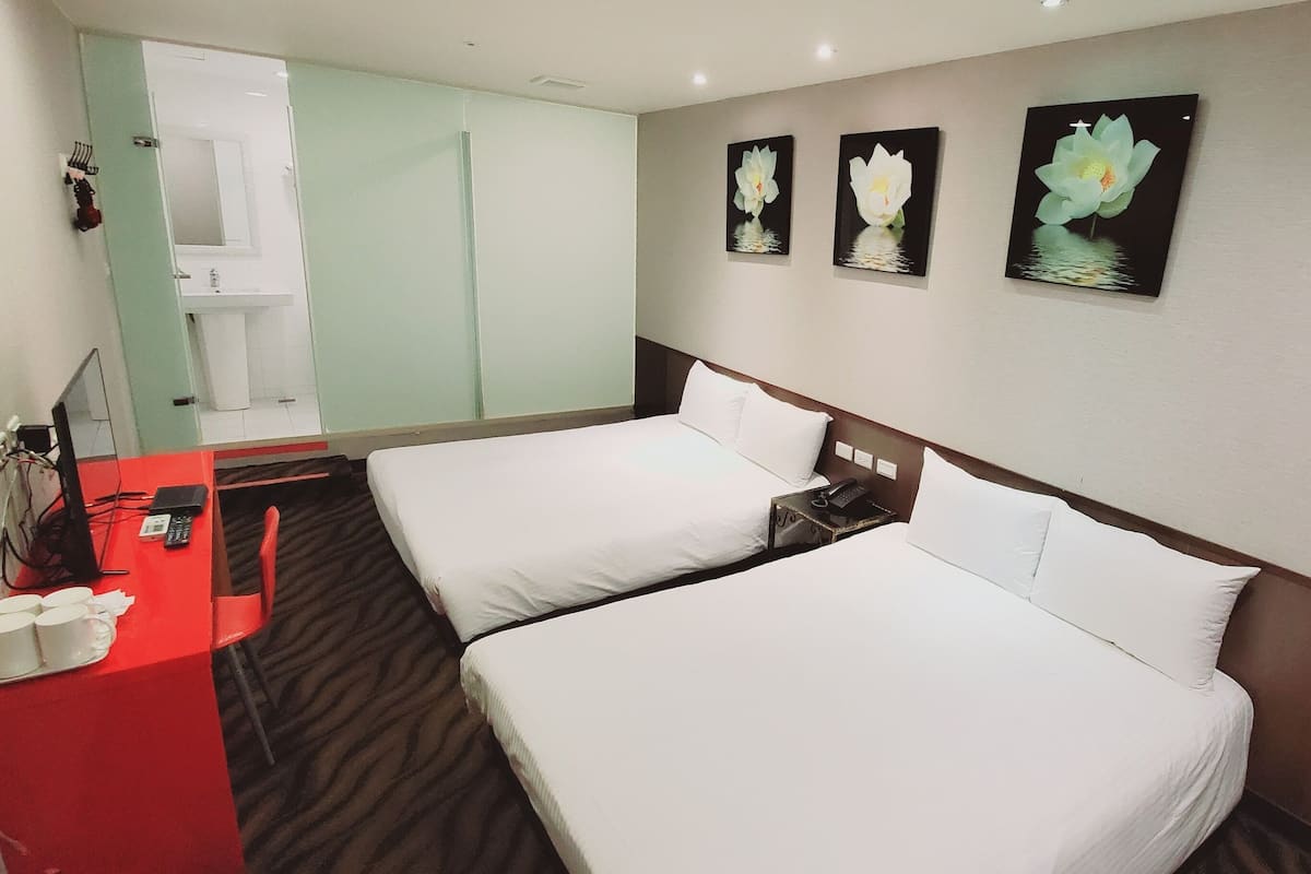 A hotel room with two beds, a desk with a telephone, and a mirror.