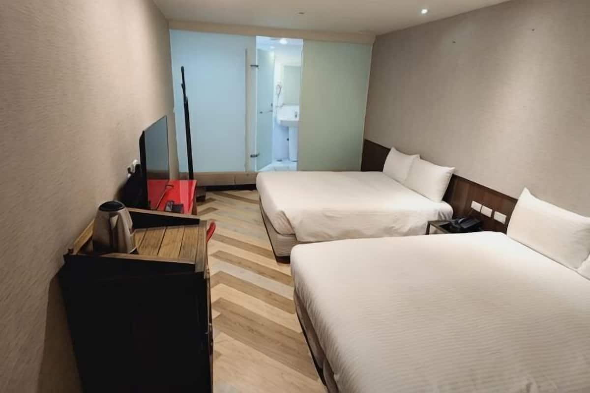 A hotel room with two beds, a TV, a desk with a chair, and a wardrobe.