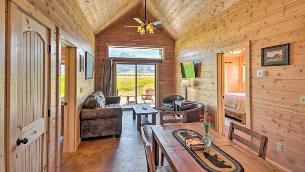 A cozy cabin interior with a wooden ceiling, a sofa, a dining table, and a view of the outdoors. - Dreamy Mountain-View Cabin Near Yellowstone! (Livingston)