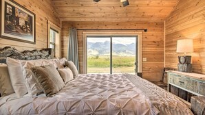 A wooden cabin bedroom with a bed, a ceiling fan, a view of mountains, and a rustic dresser. - Dreamy Mountain-View Cabin Near Yellowstone! (Livingston)