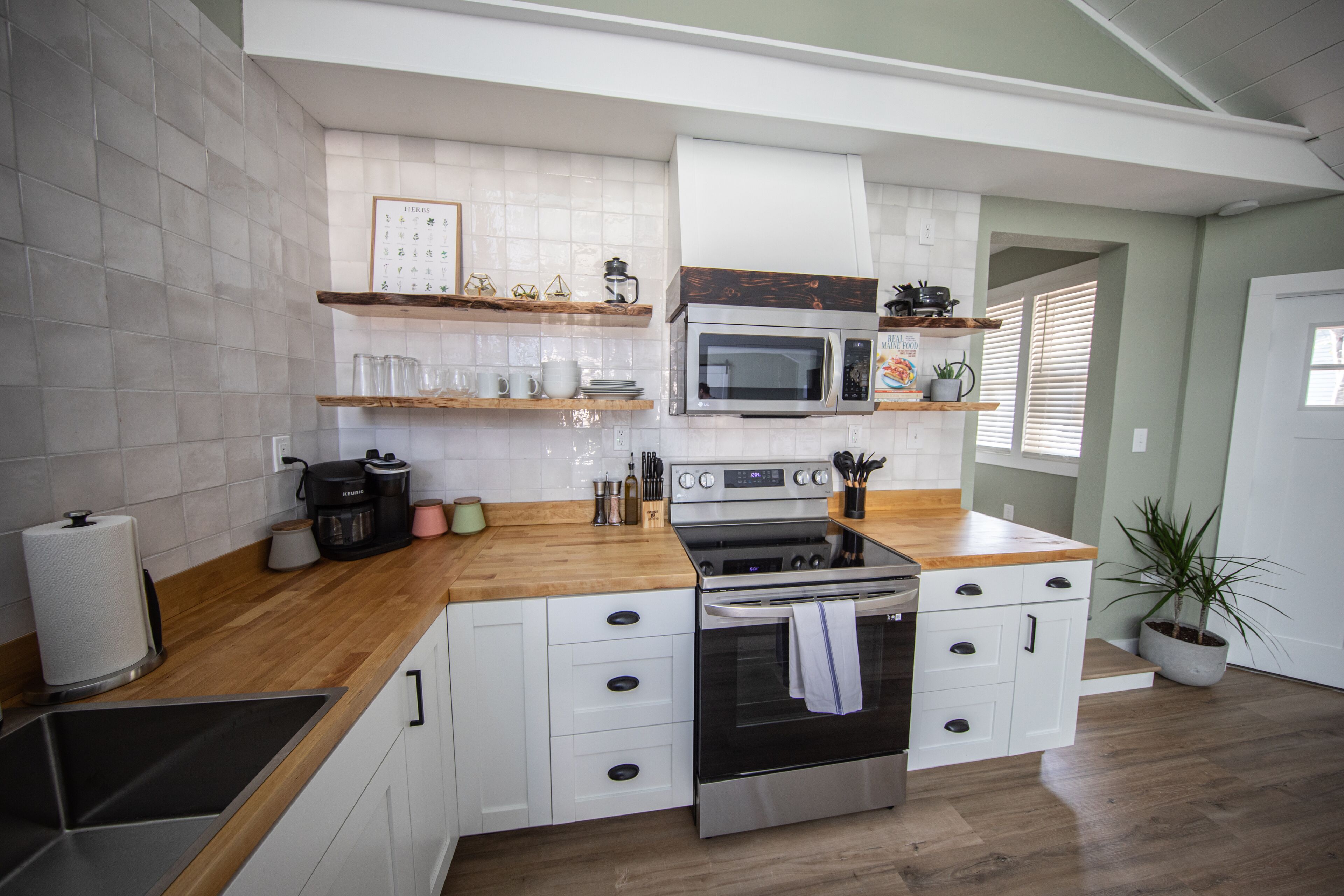 A kitchen with white cabinets, a wooden countertop, a stainless steel oven, and a microwave.