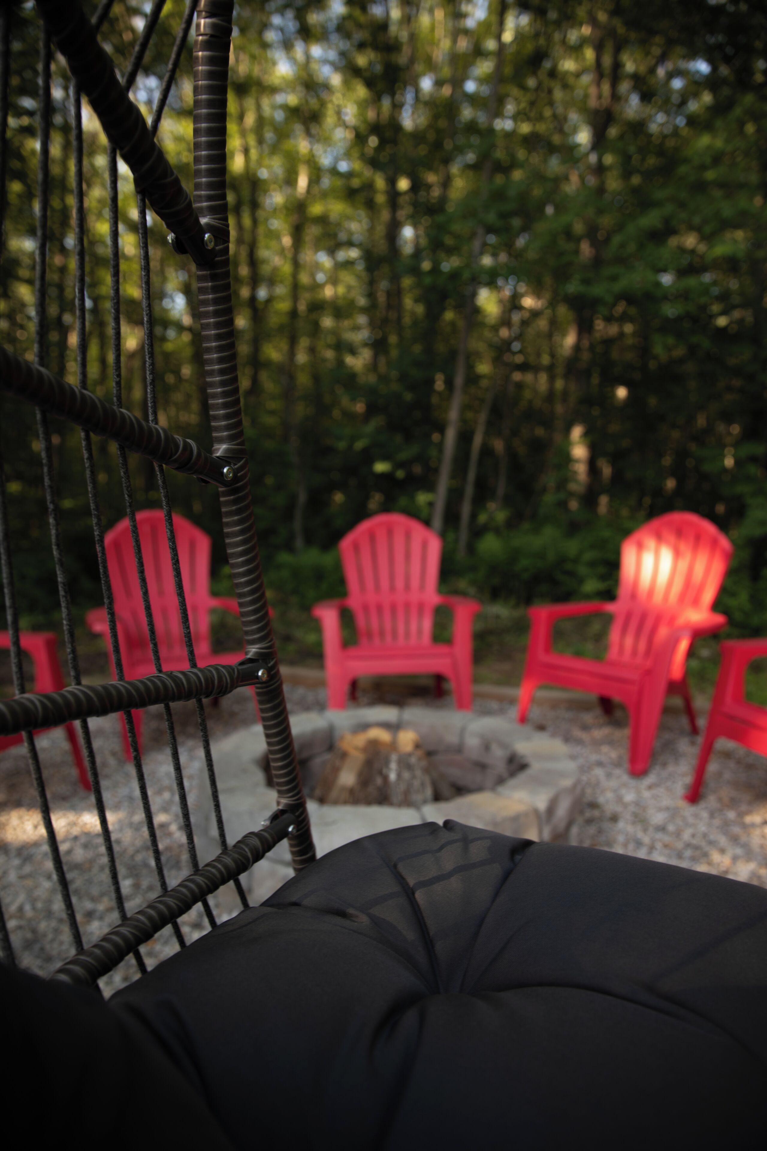 A wicker chair with a black cushion, red Adirondack chairs, and a forest background.