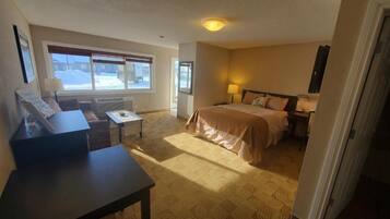 A hotel room with a bed, a desk, a chair, a window with a view, and a door.