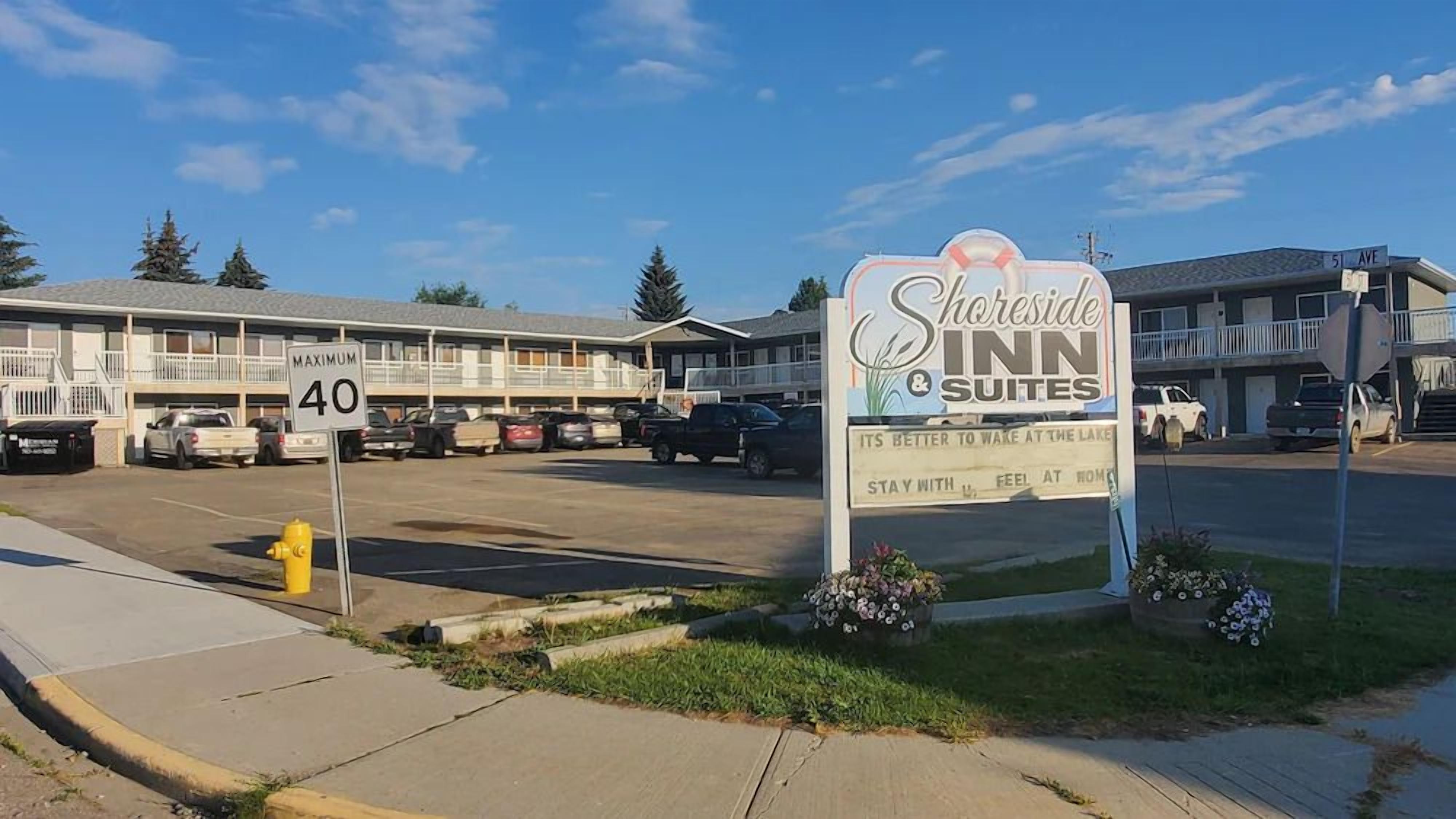 A motel with a signboard for Shoreline Inn & Suites, a parking lot, and a building with a balcony.