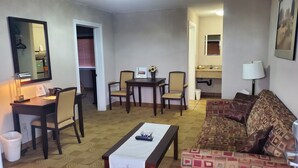 A compact living room with a sofa, a coffee table, a dining table with chairs, a small kitchen area, and a mirror on the wall. - Shoreside Inn & Suites (Wabamun)