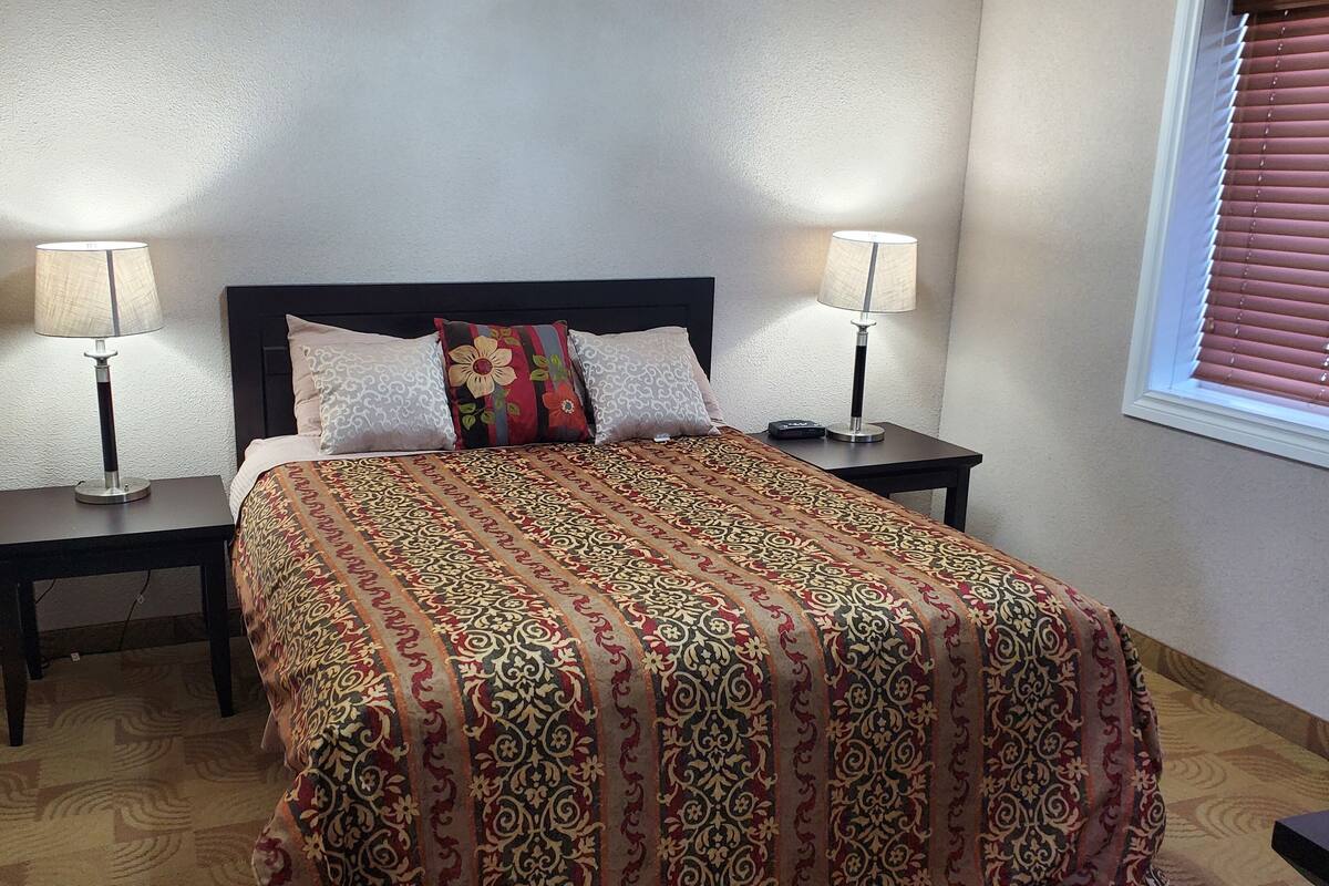 A bedroom with a bed, two nightstands, two lamps, and a window with blinds.
