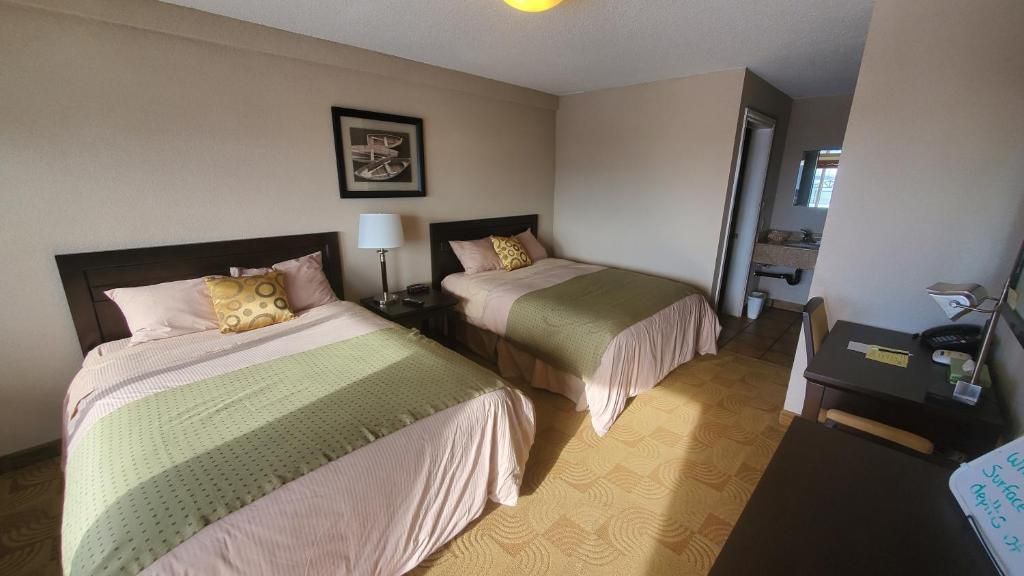 A hotel room with two beds, a desk, a chair, a lamp, and a framed picture on the wall.