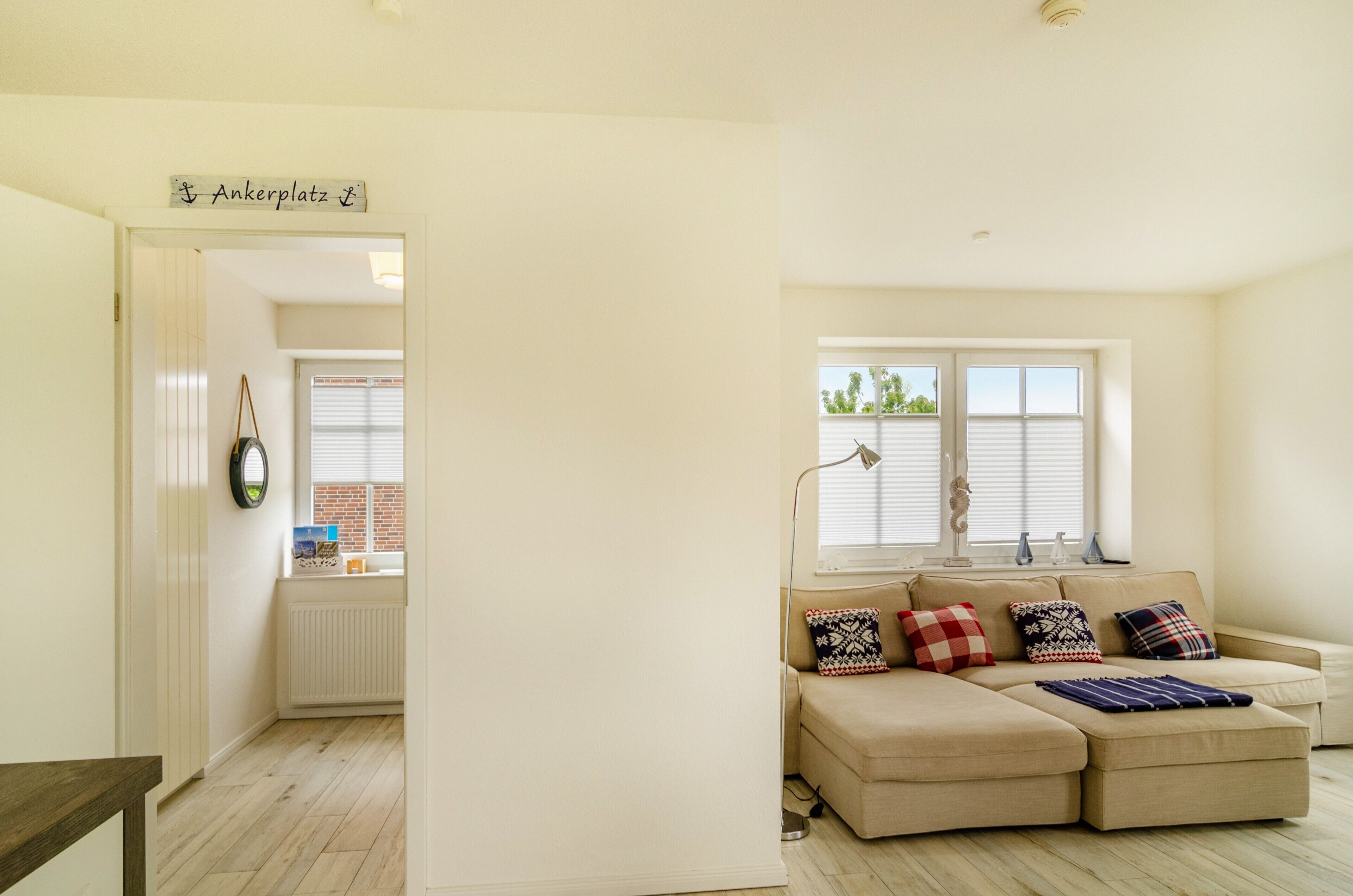 Una sala de estar con un sofá color beige, cojines estampados, una ventana con persianas y un cartel sobre la puerta.