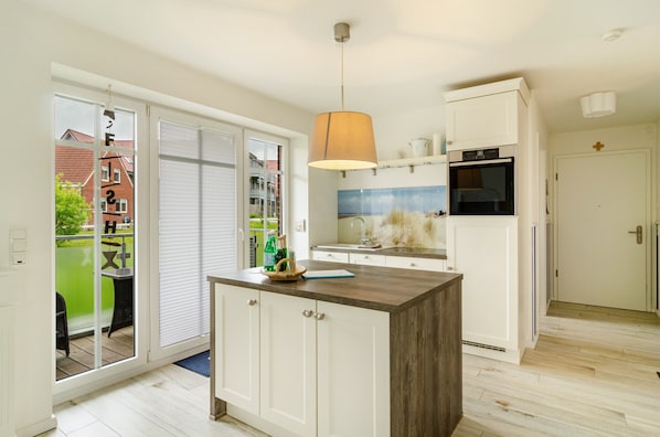 A modern kitchen with a central island, a built-in oven, and a large window overlooking a green outdoor area.