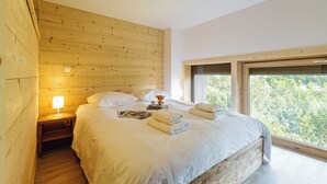 A bedroom with a wooden headboard, a bedside table with a lamp, a bed with white linens, and a window with a view of trees. - Grand Roc A216 150m from Slopes, Mont-Blanc View & Parking, Argentière (Chamonix), France (Argentière (Chamonix))