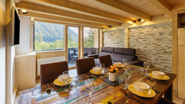 A wooden dining table set with plates, glasses, and cutlery, with a stone wall and a view of mountains in the background. - Grand Roc A216 150m from Slopes, Mont-Blanc View & Parking, Argentière (Chamonix), France (Argentière (Chamonix))