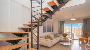 A modern living room with a wooden staircase, a sofa set, a coffee table, and a view through the glass door. - Family Duplex Riviera With Pool, Mijas Costa, Spain (Mijas Costa)