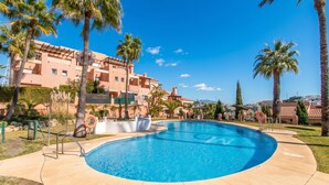 A swimming pool with a curved edge, surrounded by palm trees and a building with balconies. - Family Duplex Riviera With Pool, Mijas Costa, Spain (Mijas Costa)