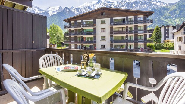 Een balkon met een tafel gedekt voor twee personen, stoelen en uitzicht op een berg.