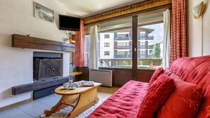 Een woonkamer met een rode bank, een open haard, een televisie en uitzicht op een gebouw door een schuifdeur.