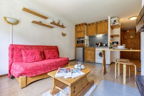 Um espaço compacto para viver com sofá vermelho, móveis de madeira, área de cozinha com armários de madeira e máquina de lavar.