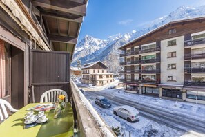 A balcony with a table set for dining, overlooking a snowy street and mountains.