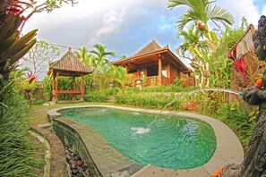 A pool surrounded by lush greenery and traditional wooden structures.