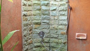A stone shower enclosure with a built-in seat and a pebble-filled basin. - Vinarya Villa (Tegallalang)