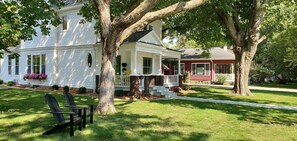 A two-story house with a porch, large trees, and a lawn.