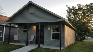 A single-story house with a gabled roof, a front porch with two chairs, and a small front yard. - New 1 bedroom cottage right off Route 66. (Galena)