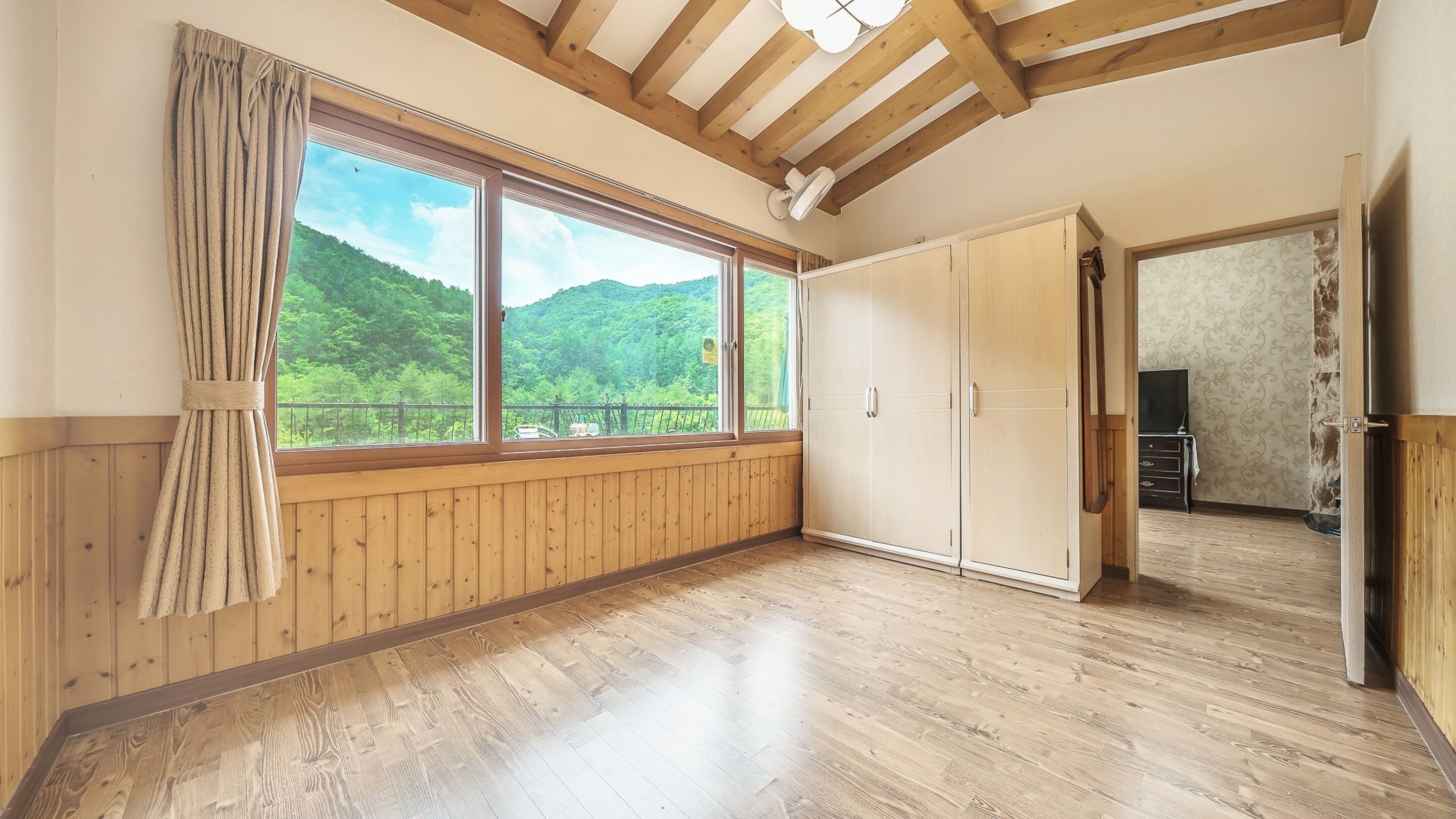 A room with wooden paneling, a large window with a view of green hills, and a wardrobe.