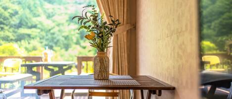A dining table with a woven vase containing flowers, set against a backdrop of greenery.