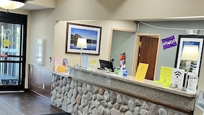 A reception area with a stone counter, a ceiling with wooden beams, a mounted television, and a fire extinguisher. - White Pine Lodge (Salamanca)