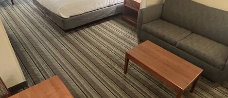 Una habitación de hotel con cama, sofá, mesa de madera y lámpara.