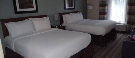 A hotel room with two single beds, a window with curtains, and a framed picture on the wall.