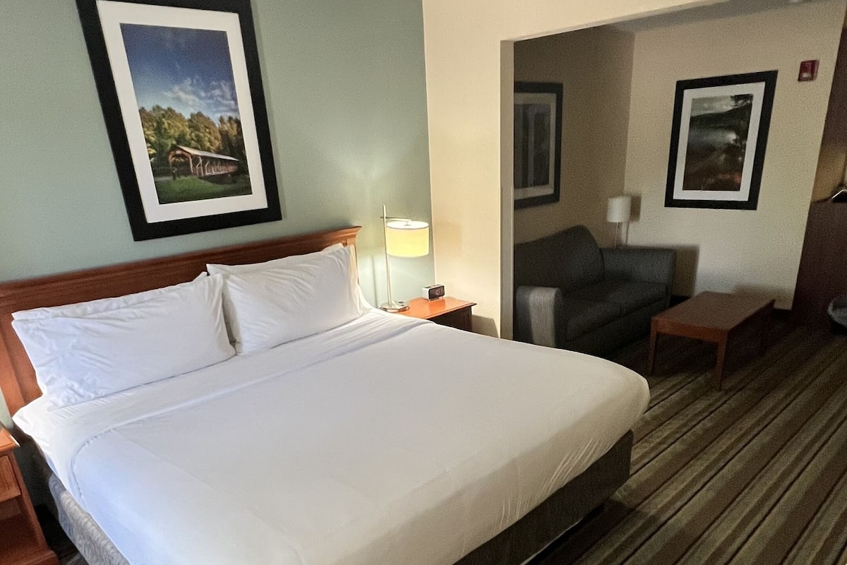 A hotel room with a large bed, a desk, a chair, and two framed pictures on the walls.