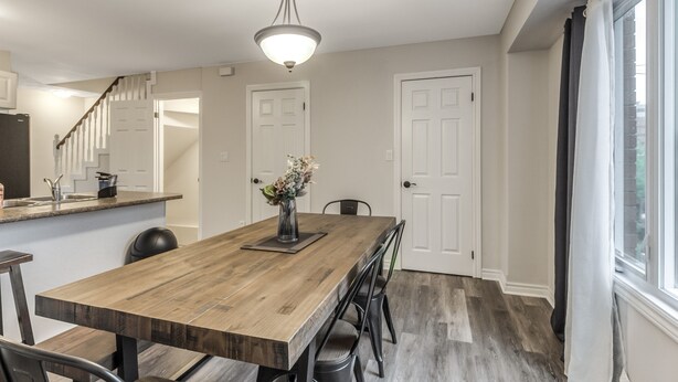 A spacious dining area with a wooden table and chairs, a vase with flowers, and a ceiling light fixture.