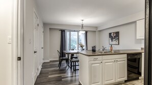 A modern kitchen with white cabinets, a built-in dishwasher, and a dining area with a table and chairs.