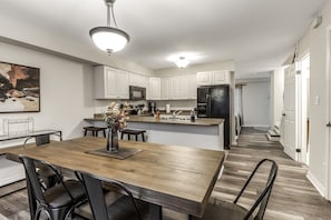 Une cuisine moderne avec des meubles blancs, une table à manger en bois et un réfrigérateur noir.