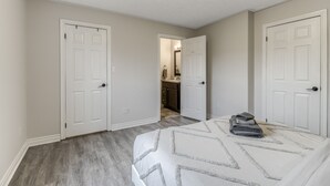 A bedroom with a bed, two white doors, a hallway, and a bathroom visible in the background.