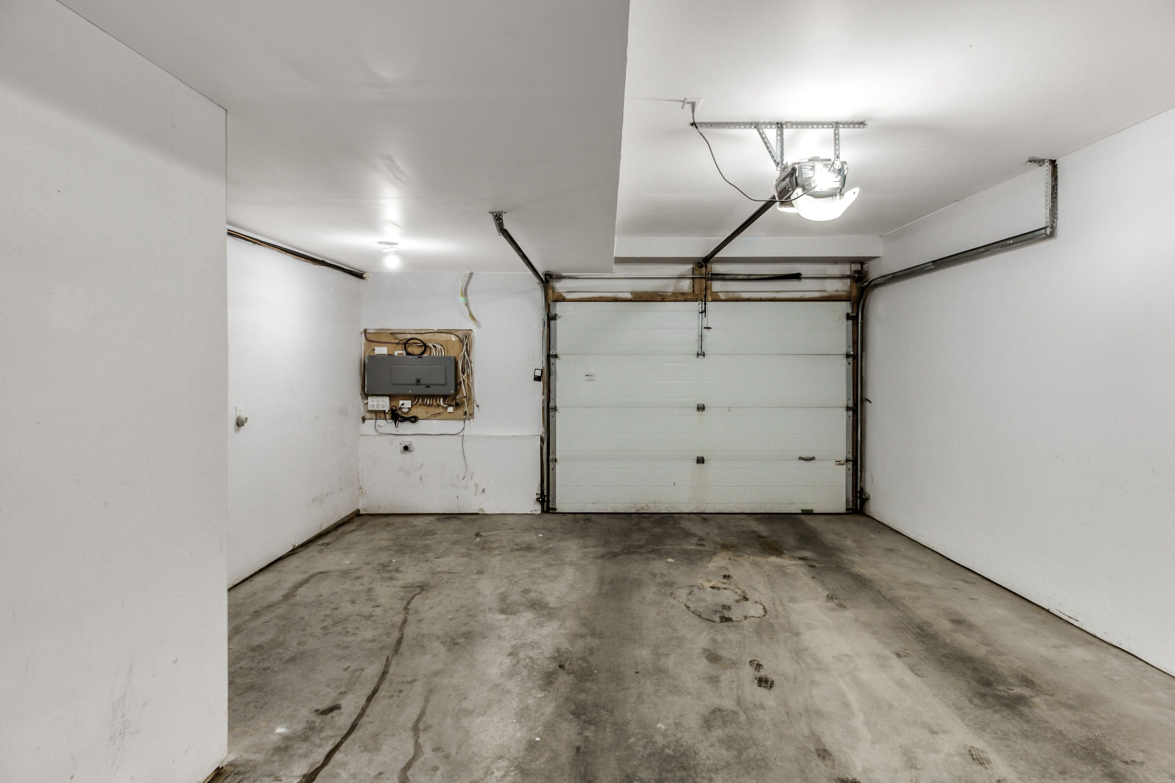 Uma garagem com chão de concreto, paredes brancas e porta fechada.