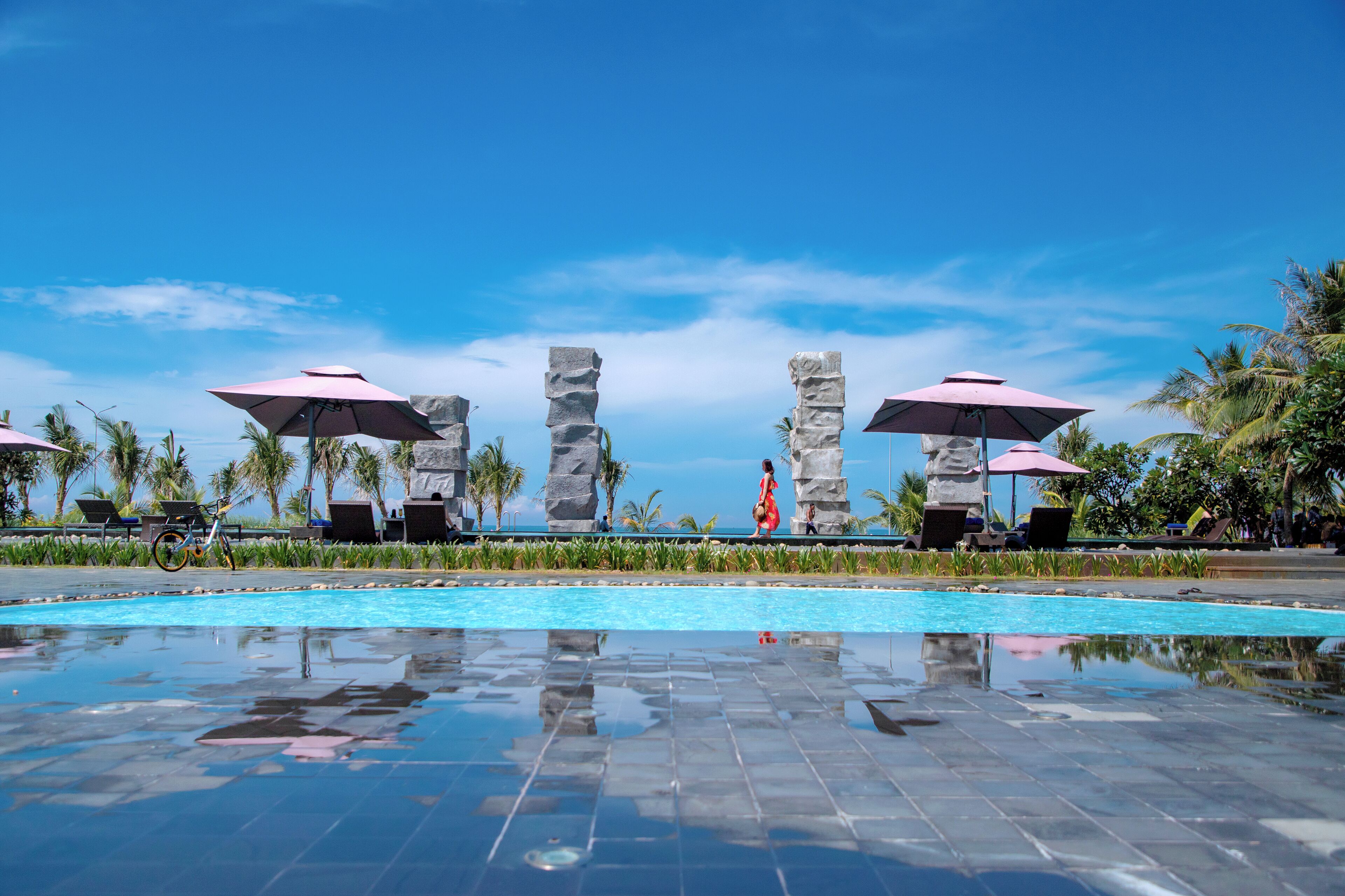 Una piscina con colonne in pietra e ombrelloni, circondata da palme e lettini.