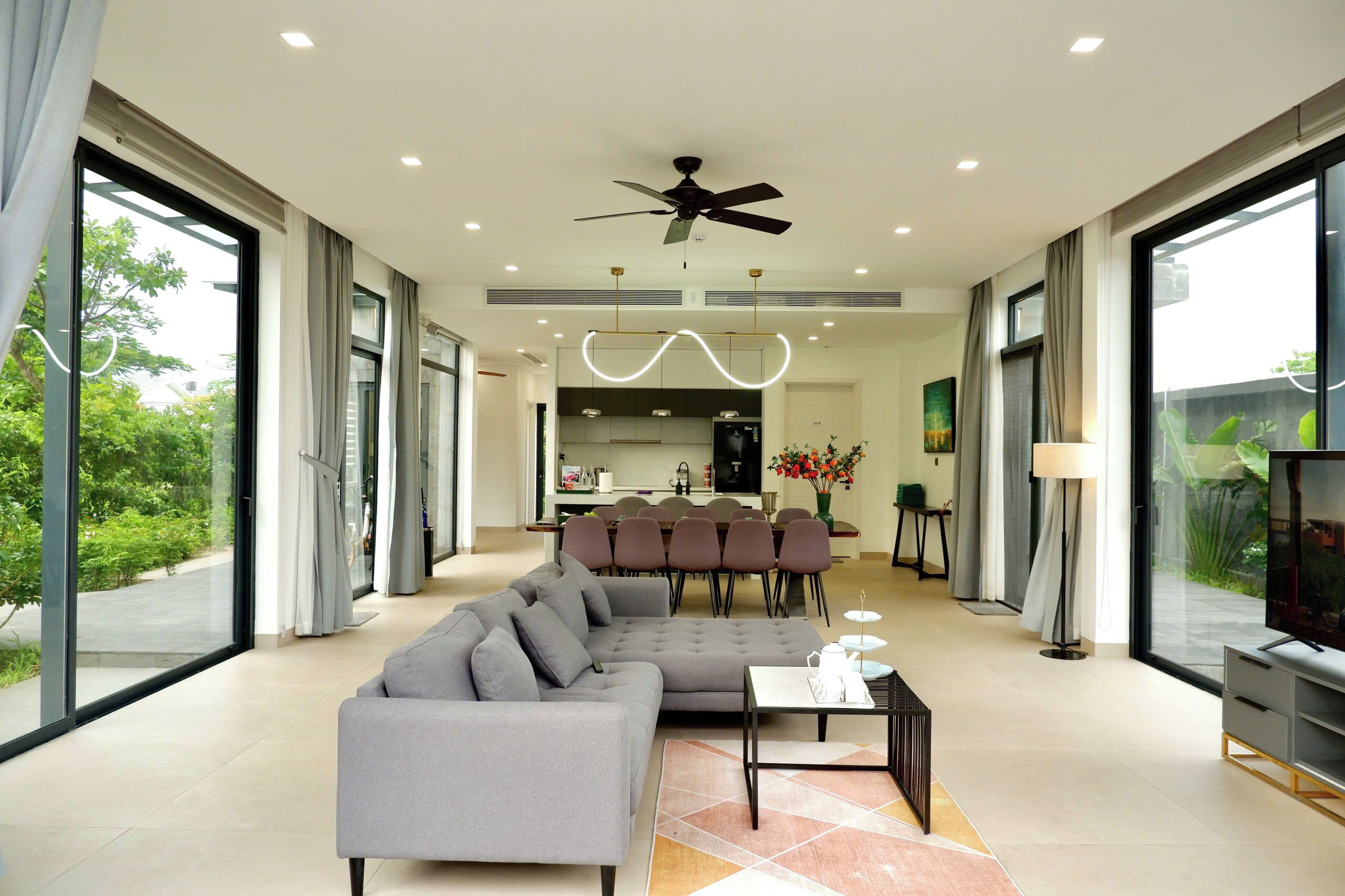 A modern living room with a sectional sofa, a coffee table, and a TV. There is a dining area with chairs and a table in the background.