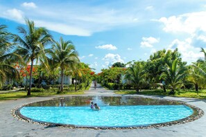 A swimming pool surrounded by palm trees and greenery, with a clear sky above. - Perolas Villas Resort - Ke Ga Bay (Tan Thanh)