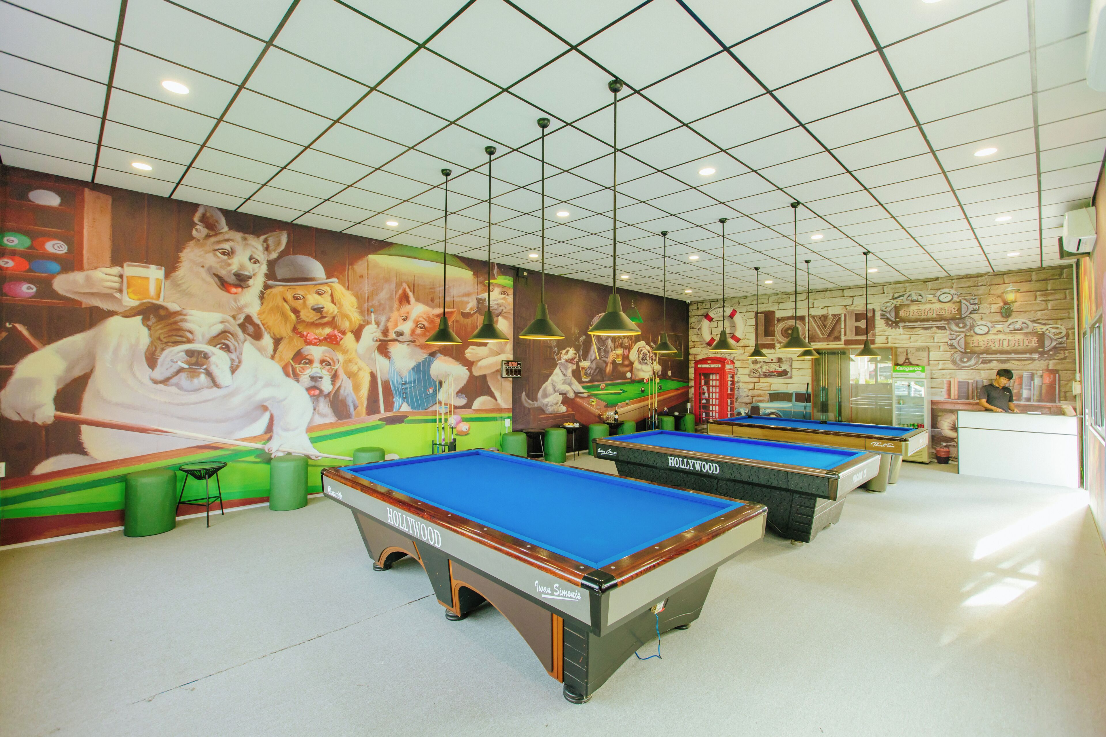 A pool hall with multiple pool tables, green stools, and a mural of dogs playing pool.
