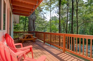 A wooden deck with a picnic table and red chairs, surrounded by tall trees. - Serene getaway with private sauna, deck, grill, balcony, & washer/dryer (Gilford)