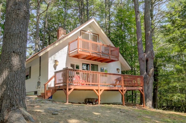 A two-story cabin with a balcony, surrounded by trees. - Serene getaway with private sauna, deck, grill, balcony, & washer/dryer (Gilford)