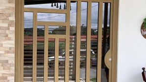 Un'ampia porta in legno con pannelli di vetro e una griglia metallica, incastonata in un edificio con pavimento piastrellato e parete in mattoni.