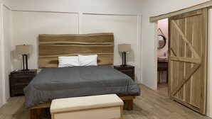 Camera da letto con una testiera in legno, una coperta grigia, due comodini con lampade, una panca e un armadio in legno.