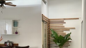 Zona pranzo con tavolo e sedie, una ventola a soffitto, una pianta in vaso e un pannello di parete in listelli di legno.