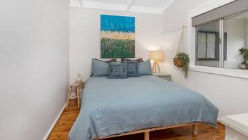 A bedroom with a bed, a hanging plant, a lamp, and a painting on the wall.