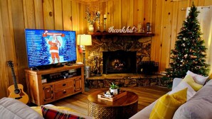 Un salon chaleureux avec une cheminée, un téléviseur diffusant un programme de Noël, une guitare et un sapin de Noël.