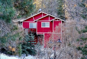 A red cabin with a balcony, surrounded by trees and snow.