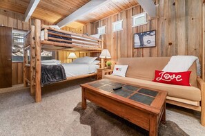 A wooden cabin interior with a bunk bed, a sofa with a 'Love' pillow, a coffee table, and a framed picture on the wall.