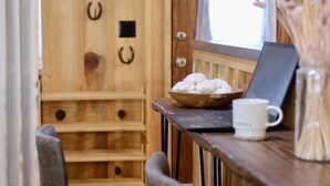 Une pièce chaleureuse aux murs en bois, avec un bureau, deux chaises, un ordinateur portable, un bol de biscuits et un vase rempli de fleurs.